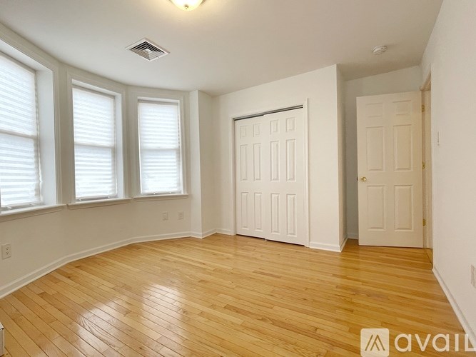 A room with wooden floors and white walls has a large white door and a window with blinds.