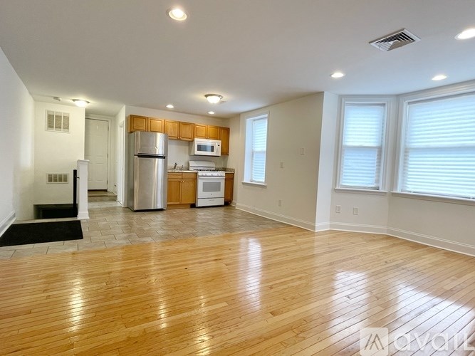 A spacious living room with wooden flooring and a kitchen area in the background.