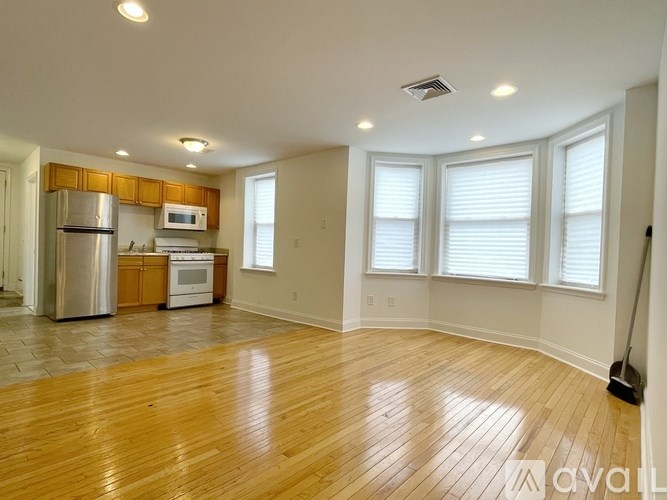 A large empty room with wooden floors and a kitchen area in the background.