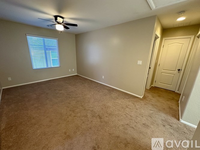 A room with a carpeted floor, a ceiling fan, and a door.