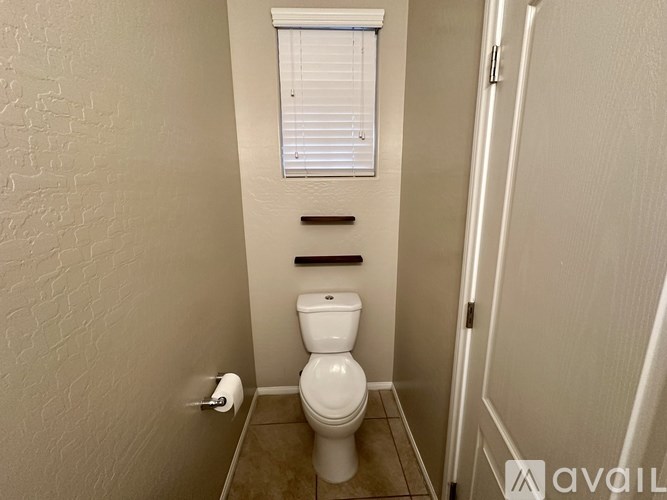 A white toilet in a small bathroom with a roll of toilet paper on the wall.
