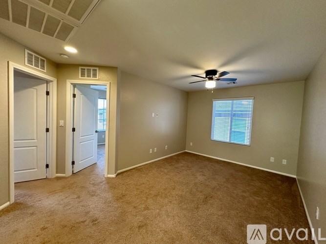 A room with a carpeted floor, a ceiling fan, and a window with blinds.