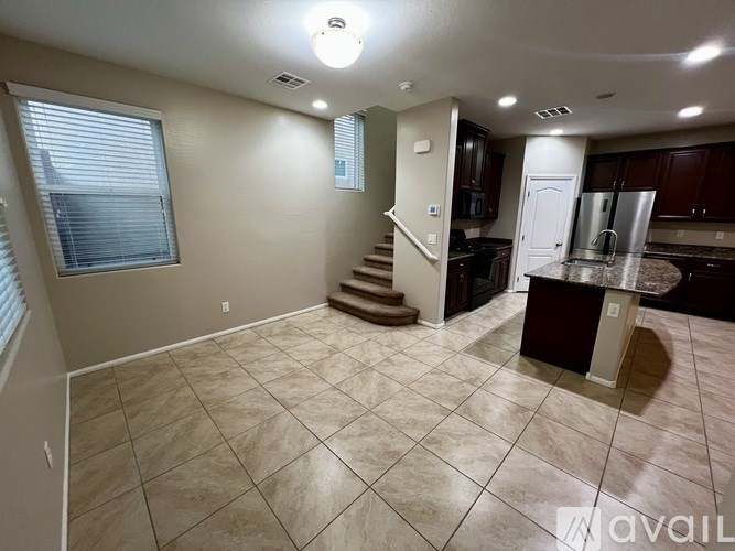 A spacious kitchen and living room with a tiled floor and a staircase leading to the upper floor.