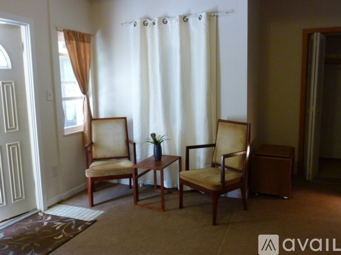 Two chairs and a table are in a room with a white curtain.