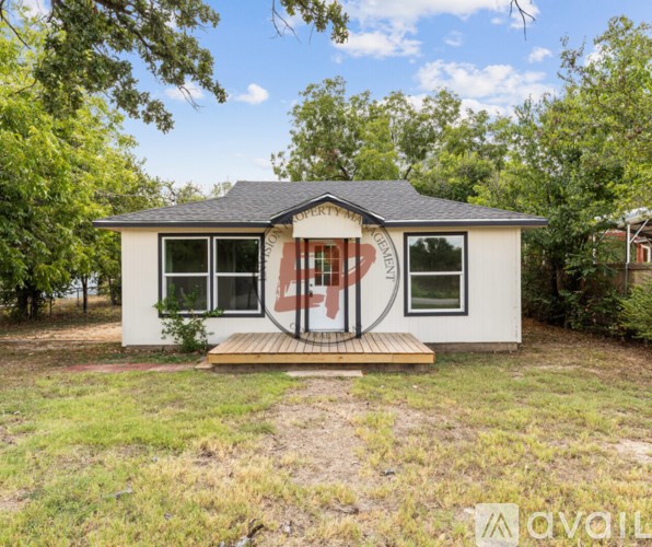 A small white house with a black roof and a wooden deck in front.