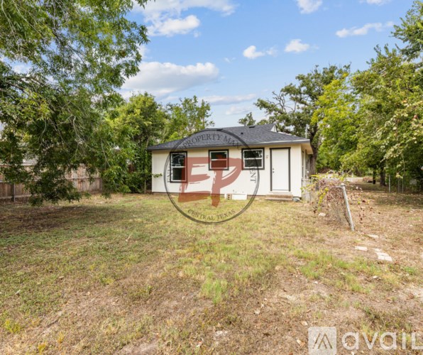 A small white house with a brown door is surrounded by trees and grass.