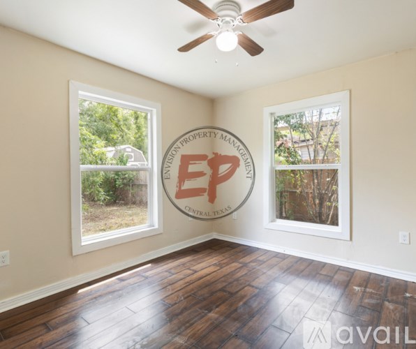 A room with a ceiling fan and two windows, one of which has a picture of a house on it.