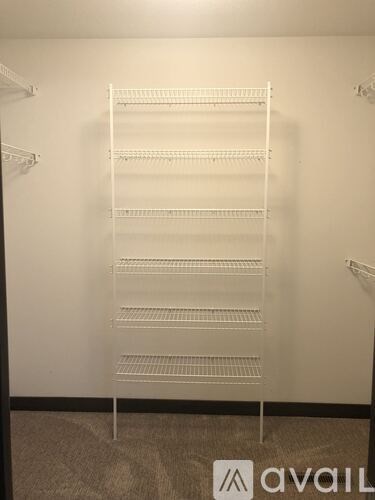 A white shelving unit with six shelves is in a room with a carpeted floor.
