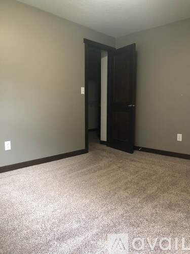 A carpeted room with a door and a light switch on the wall.