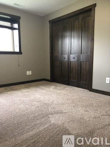 A room with a carpeted floor, a wooden wardrobe, and a window with blinds.