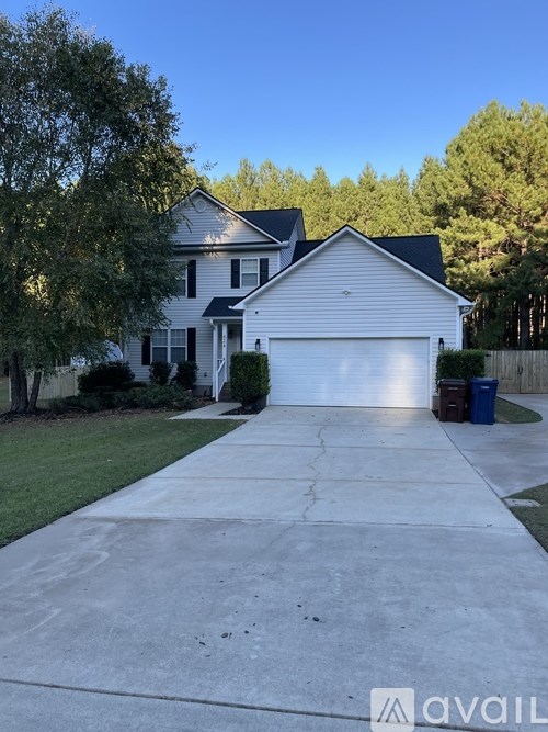 A white house with a garage is surrounded by greenery.