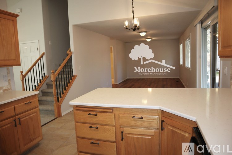 A kitchen with wooden cabinets and a countertop with a staircase in the background.