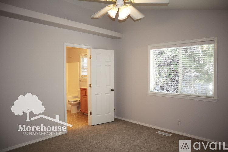 A room with a window covered by blinds, a ceiling fan, and a logo of a tree with the text "Morehouse PROPERTY MANAGEMENT" on the wall.
