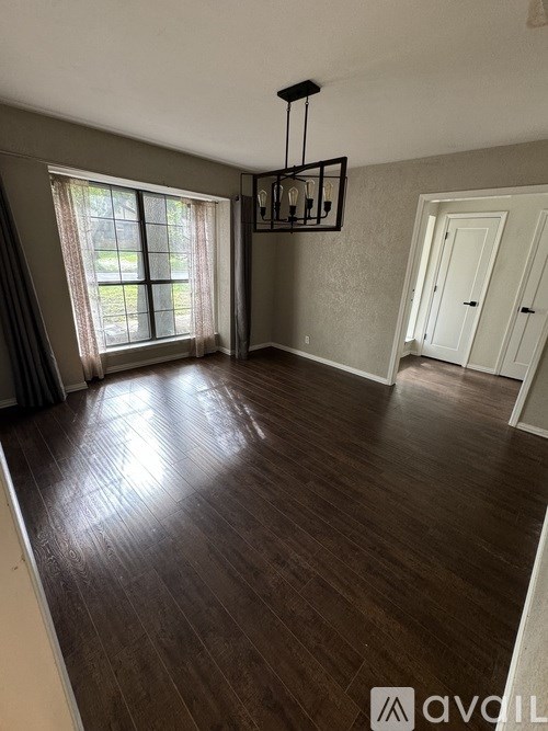 A room with wooden flooring and a large window with curtains.