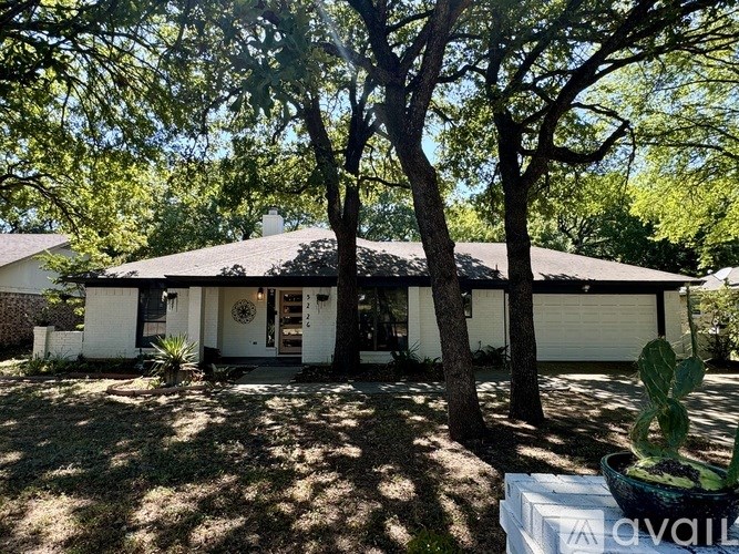 A house with a white exterior and a large front yard with a tree and a cactus.