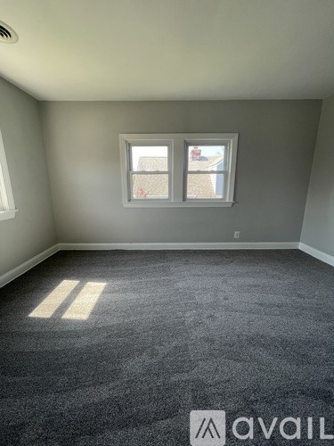 A room with grey carpet and two windows.