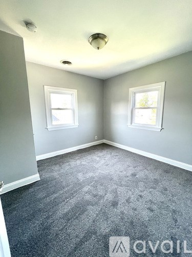 A room with grey carpet and two windows.