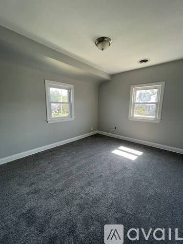 A room with grey carpet and two windows.