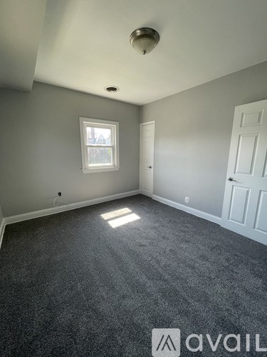 A room with grey carpet and a window letting in sunlight.