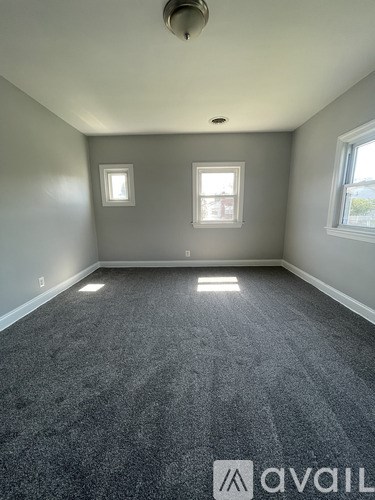A room with grey carpet and two windows.