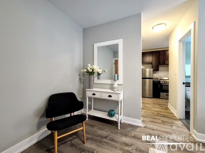 A room with a chair, a mirror, and a table with flowers on it.