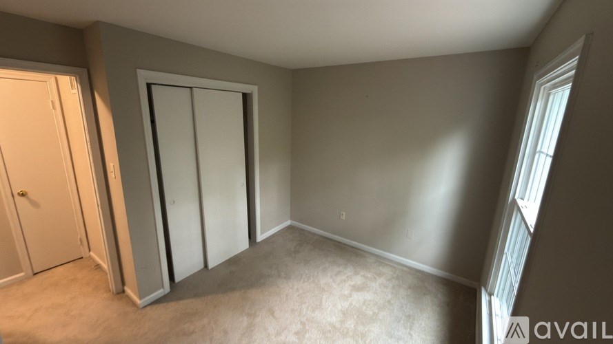 A room with a carpeted floor, a white door, a white wardrobe, and a window with blinds.