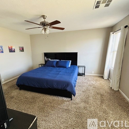 A bedroom with a blue bedspread and a ceiling fan.