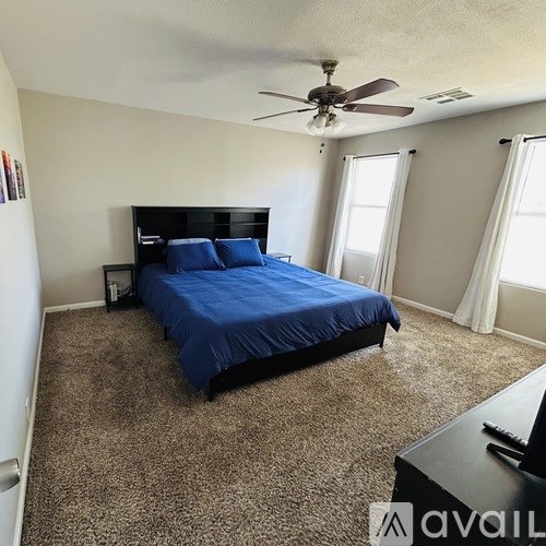 A bedroom with a blue bedspread and a ceiling fan.
