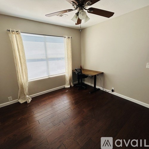 A room with a brown wooden floor and a ceiling fan.