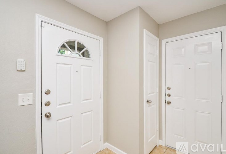 A white door with a window in the middle is in a room with a white wall.