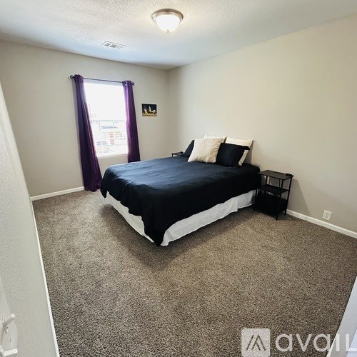 A bedroom with a bed, nightstand, and window with purple curtains.