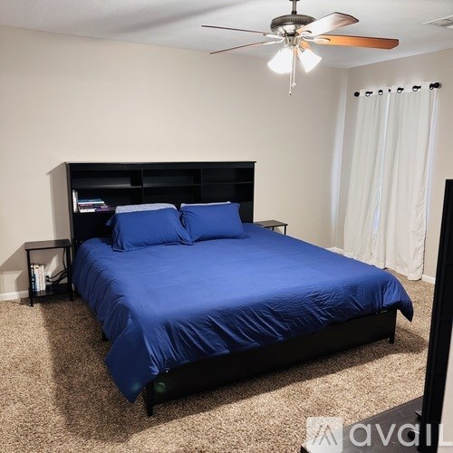 A bed with a blue cover is in a room with a ceiling fan.