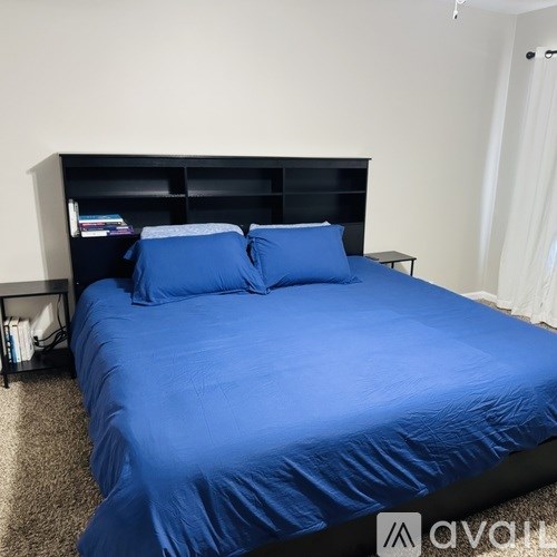 A bed with a blue comforter and two blue pillows sits in a room with a black headboard and a white wall.