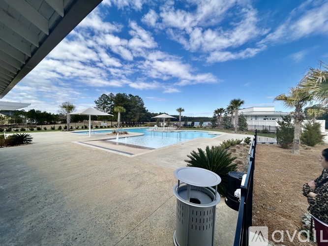 A large outdoor swimming pool surrounded by a concrete patio and a metal trash can.