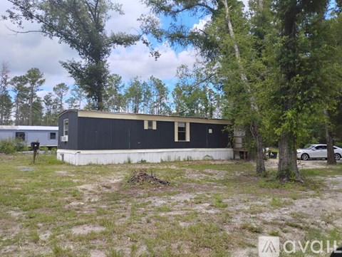 A black building with a white base is surrounded by trees and grass.