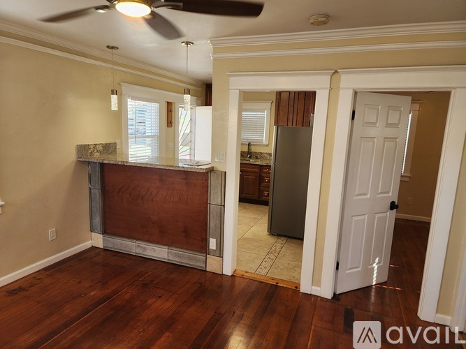 A room with a ceiling fan and a kitchen area with a refrigerator.