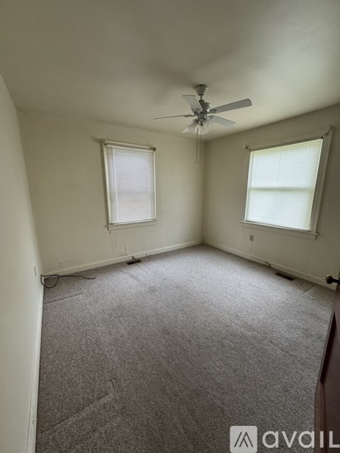 A room with a carpeted floor, a ceiling fan, and two windows.