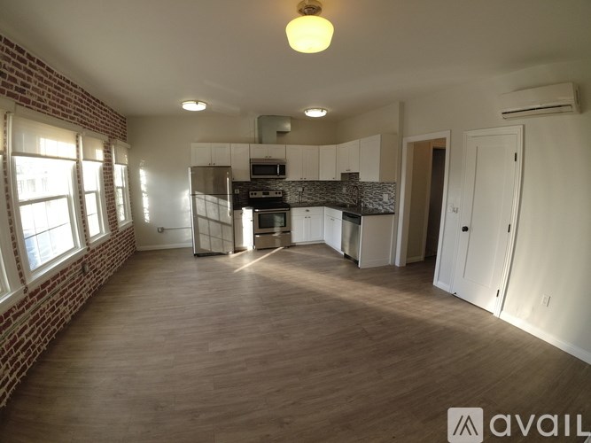 A spacious kitchen with wooden floors and a brick wall.