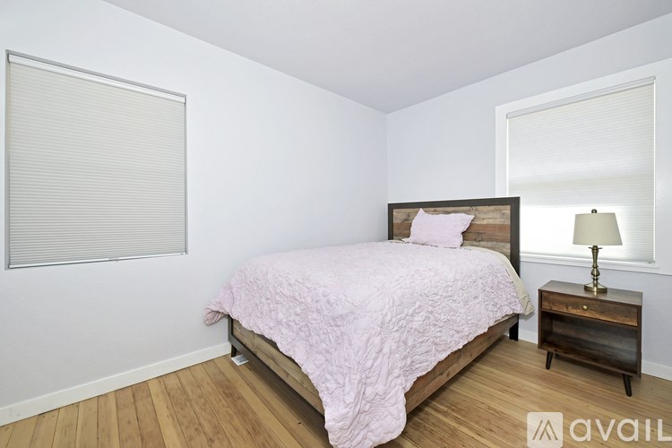 A bedroom with a pink bedspread and a wooden nightstand with a lamp.