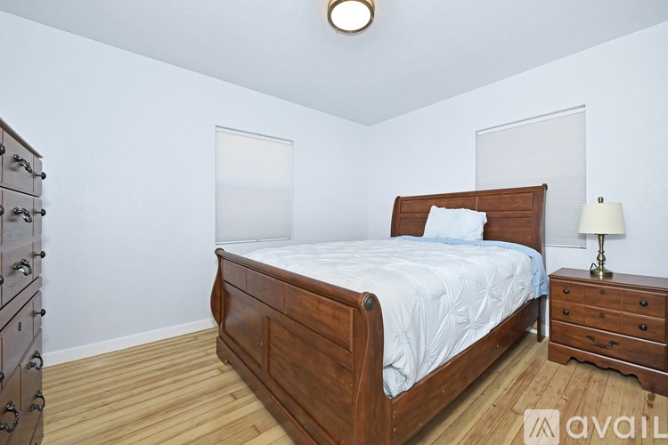 A bedroom with a large bed, a dresser, and a nightstand with a lamp.