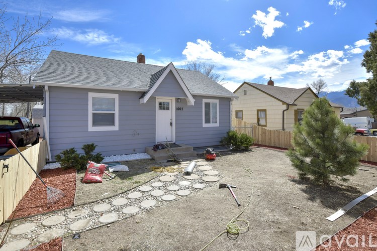 A house with a grey roof and a white door is surrounded by a fence and a small garden.