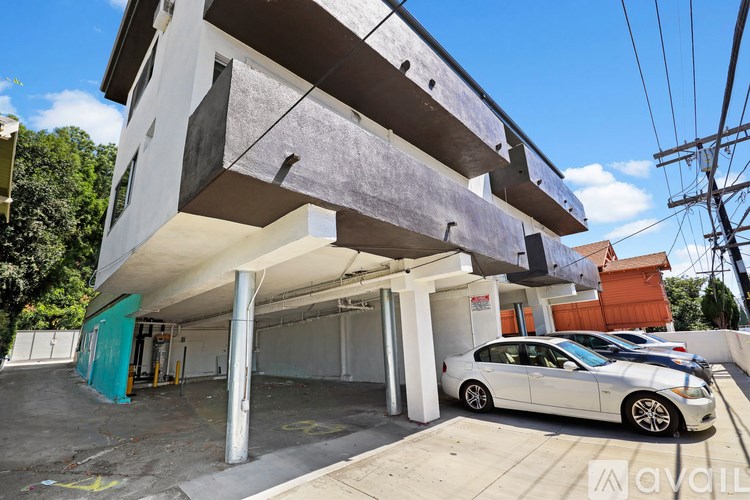 A white car is parked in a garage under a building with a blue sky in the background.