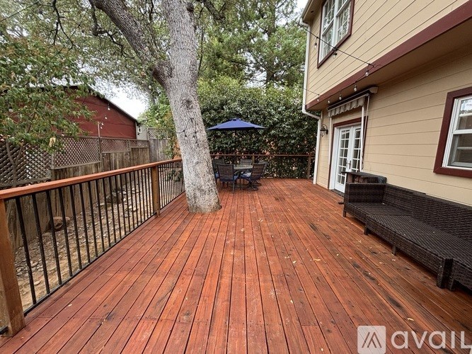 A wooden deck with a tree and a black umbrella.