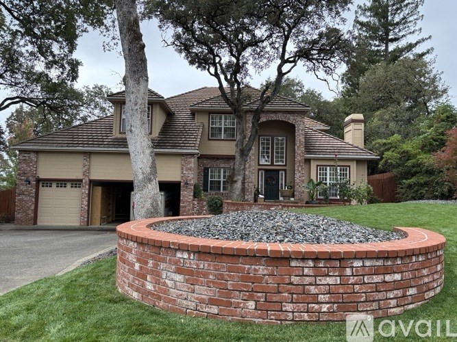 A house with a brick wall and a tree in front.