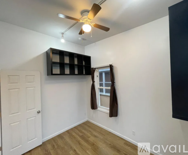 A room with a ceiling fan and a window with a brown curtain.