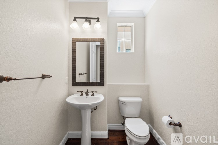 A bathroom with a toilet, sink, mirror, and light fixture.