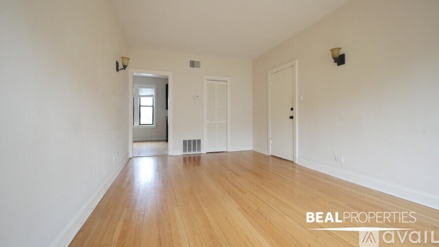 A room with wooden floors and white walls, with a door on the right and a window on the left.