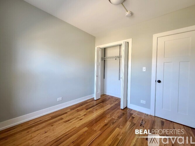 A room with wooden floors and white walls, with a door on the right and a partially open doorway on the left.