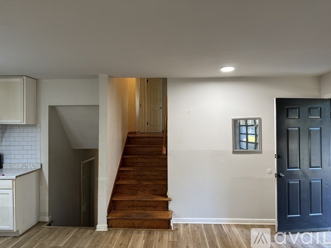 A wooden staircase leads up to a door in a white room.