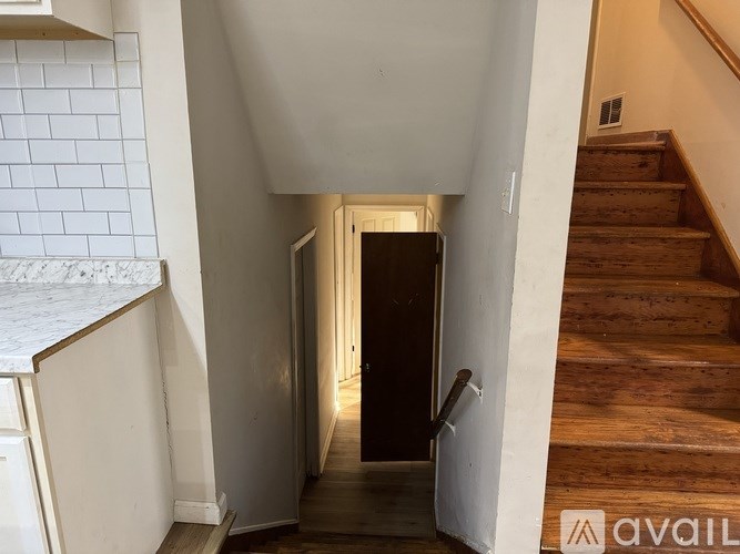 A hallway with a wooden staircase on the right and a white tiled wall on the left.
